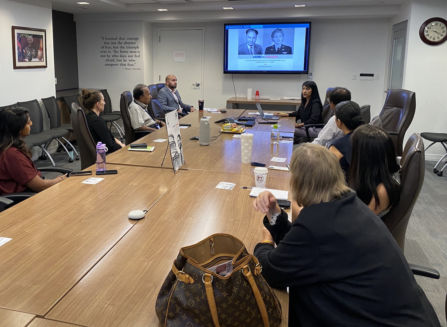 filmmaker Mridu Chandra presents the story of the film Saund vs Cochran. she is seated at a office conference table with about 10 others in the room.